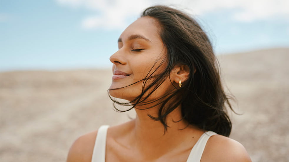 A portrait of a young woman outdoors enjoying a calming breeze moving her hair against a blue sky and natural background